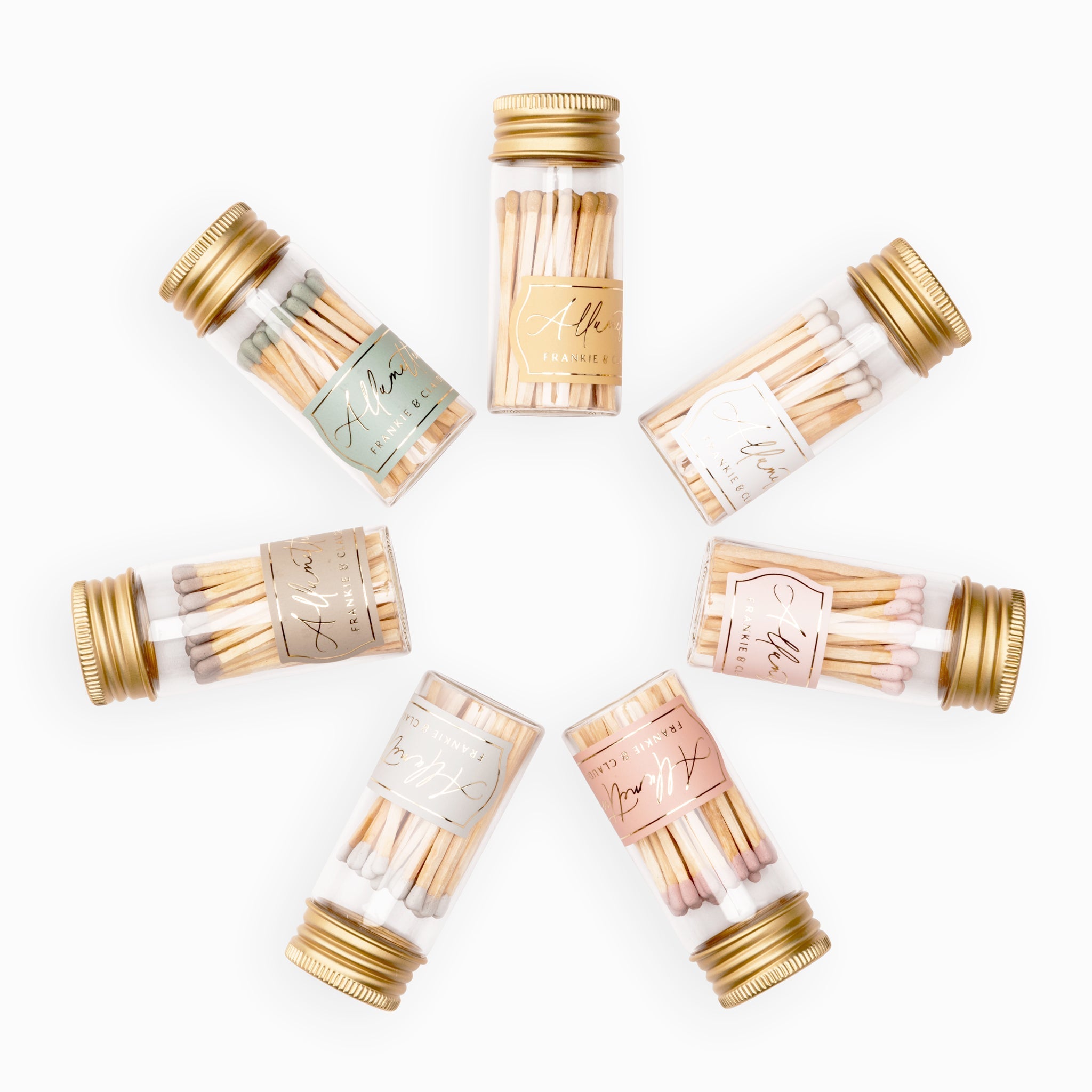 Assorted Frankie & Claude Allumette Match Jars arranged in a circular pattern, showcasing a variety of match tip colors including blush pink, classic white, dusty rose, blush pink, sage green, and honey gold in clear glass jars with golden lids.